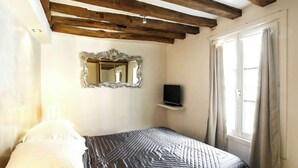 Una camera da letto con un letto, uno specchio, una televisione e una finestra con tende.
