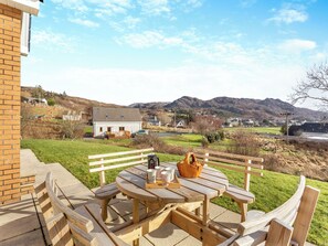 A wooden picnic table with benches, a basket, and cups on a patio overlooking a village and mountains. - Welcome to Bramble Cottage. (Gairloch)