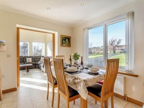 A dining area with a table set for four, a sofa in the background, and a large window with a view of the outdoors. - Welcome to Bramble Cottage. (Gairloch)