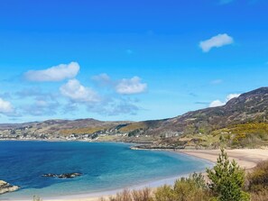 A coastal landscape with a beach, clear blue sky, and distant hills. - Welcome to Bramble Cottage. (Gairloch)