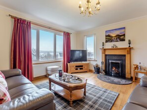 A living room with a fireplace, television, sofa, and large windows. - Welcome to Bramble Cottage. (Gairloch)