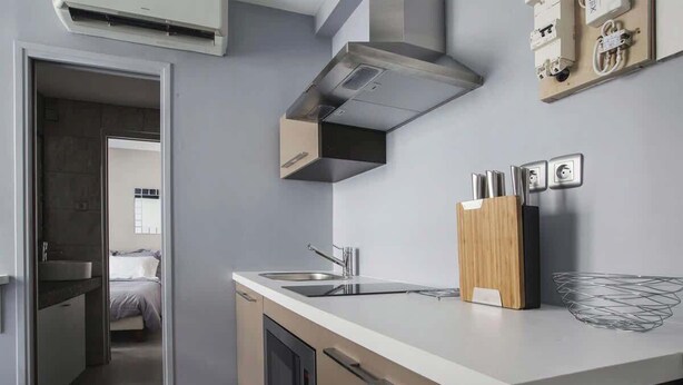 A modern kitchen with a built-in oven, microwave, and stainless steel range hood. There is a wooden cutting board and a metal bowl on the counter.