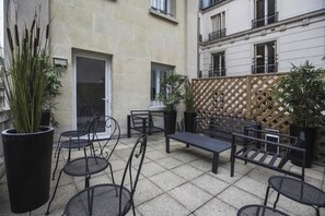 Un patio al aire libre con mobiliario metálico, plantas en macetas y una cerca de listones de madera.