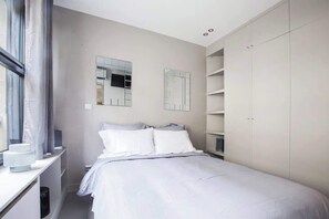 Un dormitorio moderno con cama, armario, espejo y ventana con cortinas.