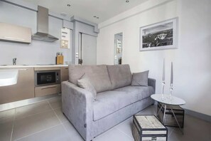 A modern kitchen with a grey sofa, a small round table, and a framed picture on the wall.