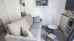 A modern living room with a grey sofa, a small round table, and a television mounted on the wall.