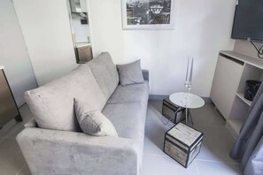A modern living room with a grey sofa, a small round table, and a television mounted on the wall.