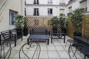 An outdoor patio with a wooden lattice wall, black metal furniture, and potted plants.