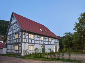 Ein traditionelles Fachwerkhäuschen mit einem steilen roten Dach, zahlreichen Fenstern und einem gepflegten Garten.