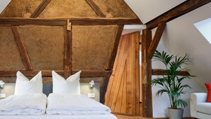 Une chambre avec un plafond en bois, un lit avec une literie blanche, une plante en pot et un coussin rouge sur un canapé.