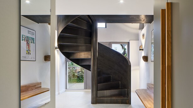 Un intérieur moderne avec un escalier en colimaçon, un banc en bois et un tableau encadré au mur.