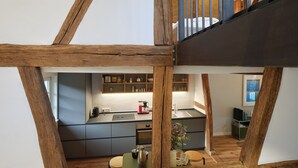 Une cuisine moderne avec des poutres en bois, un coin repas avec une table et des chaises, et une vue sur une chambre à coucher avec un lit.