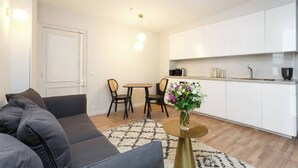 Ein modernes Wohnzimmer mit einer Couch, einem Esstisch mit Stühlen, einer Küchenzeile mit weißen Schränken und einer Vase mit Blumen auf einem Tisch.