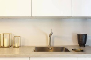 A modern kitchen with a stainless steel sink, two glass candle holders, and a dark ceramic cup on the countertop.