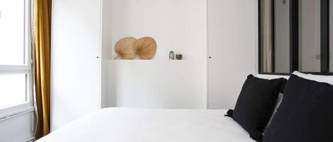 A bedroom with a large bed, a wardrobe, and a window with curtains.