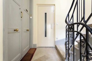 Um corredor com uma porta branca, um tapete de entrada vermelho e uma escada de metal preta.