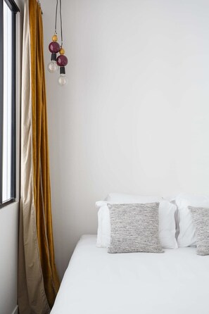 A bedroom with a bed, white bedding, a textured pillow, and a curtain.
