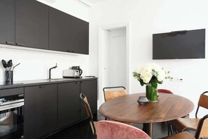 A modern kitchen with dark cabinets, a round wooden table, and a flat-screen TV mounted on the wall.