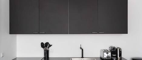 A modern kitchen with dark cabinets, a stainless steel sink, and a coffee maker.