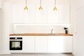 Eine moderne Küche mit weißen Schränken, einer Holz Arbeitsplatte, einem eingebauten Backofen und drei Pendelleuchten.