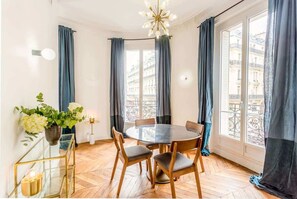 Ein Essbereich mit einem runden Tisch, Stühlen, einer Blumenvase und Blick auf Gebäude durch große Fenster.