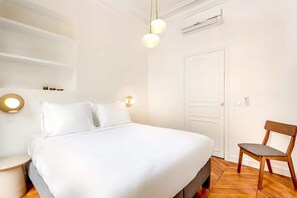 A hotel room with a large bed, a wooden chair, and a white door. - Elegant spacious apartment with balcony near Opéra - 2 bedrooms - A/C - Steps from the grands magasins - Quatre Septembre by Habitat Parisien (Paris)