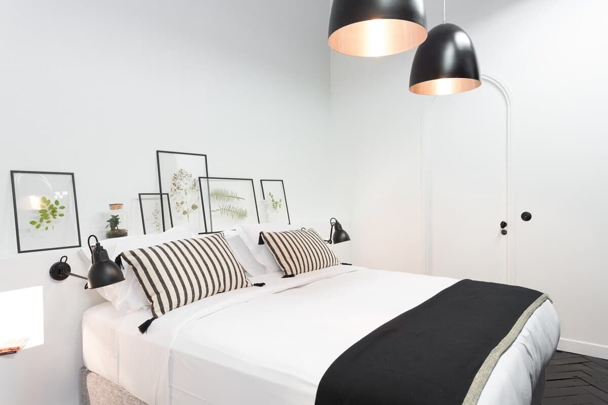 A neatly arranged bedroom with a bed, black and white striped pillows, a black throw blanket, and black pendant lamps.