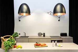 Uma cozinha moderna com duas luminárias pendentes, uma pia, uma cafeteira e uma tábua de corte com legumes.