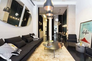 Uma sala de estar moderna com um sofá preto, uma mesa de centro redonda e iluminação pendente.