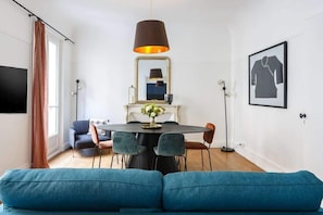 Uma sala de estar moderna com um sofá azul-turquesa, uma mesa de jantar redonda com cadeiras, um abajur preto, um espelho e uma obra de arte emoldurada na parede.