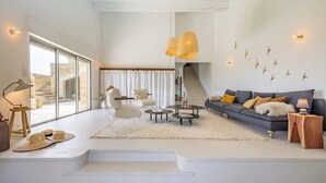 A spacious living room with a large window, a staircase, a dark sofa with cushions, and a coffee table.
