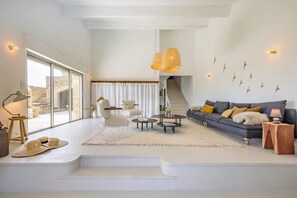 A spacious living room with a large window, a staircase, a dark sofa with cushions, and a coffee table.