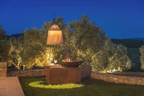 An outdoor patio area with a table lamp, a fire pit, and a stone wall.