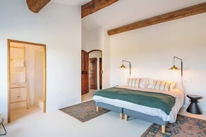 Quarto com cama, duas luminárias de cabeceira, uma escada de madeira e um tapete estampado.