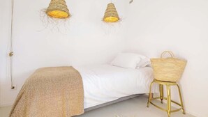 A bedroom with a bed, two hanging light fixtures, and a wicker chair.
