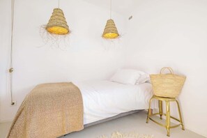 A bedroom with a bed, two hanging light fixtures, and a wicker chair.