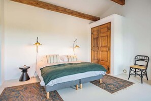 A bedroom with a bed, two bedside lamps, a wooden door, a chair, and a small table.