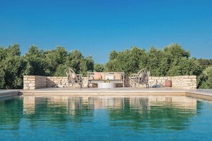 Piscina com muro de pedra e espreguiçadeiras.