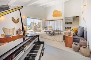A spacious living room with a grand piano, comfortable seating, and a large window offering a view of the outdoors.