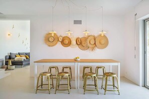 A dining area with a white table, four gold stools, and a wall decorated with hats and pendant lights.
