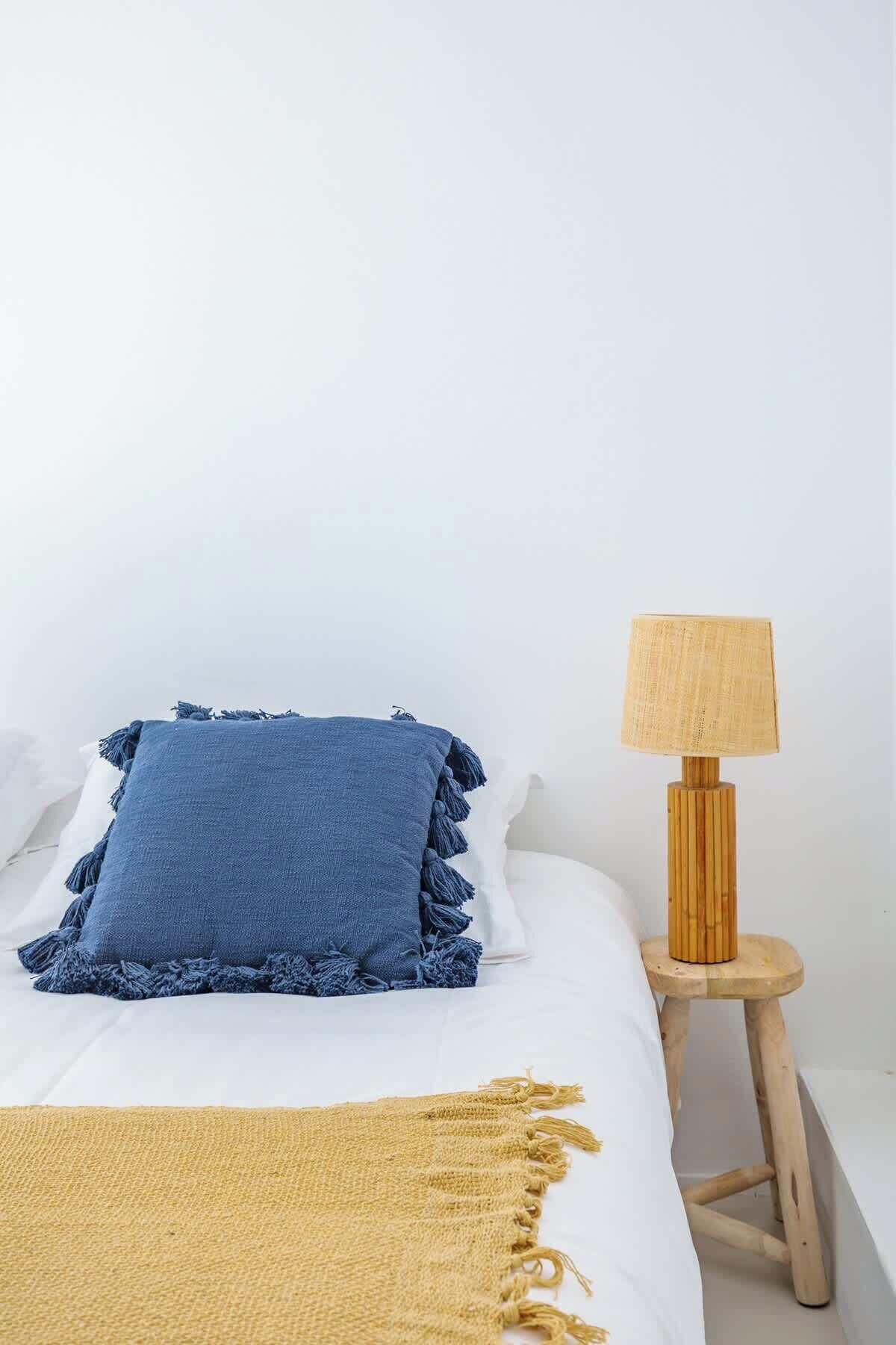 Uma cama com um travesseiro azul, um cobertor amarelo e uma mesa de cabeceira de madeira com uma luminária.