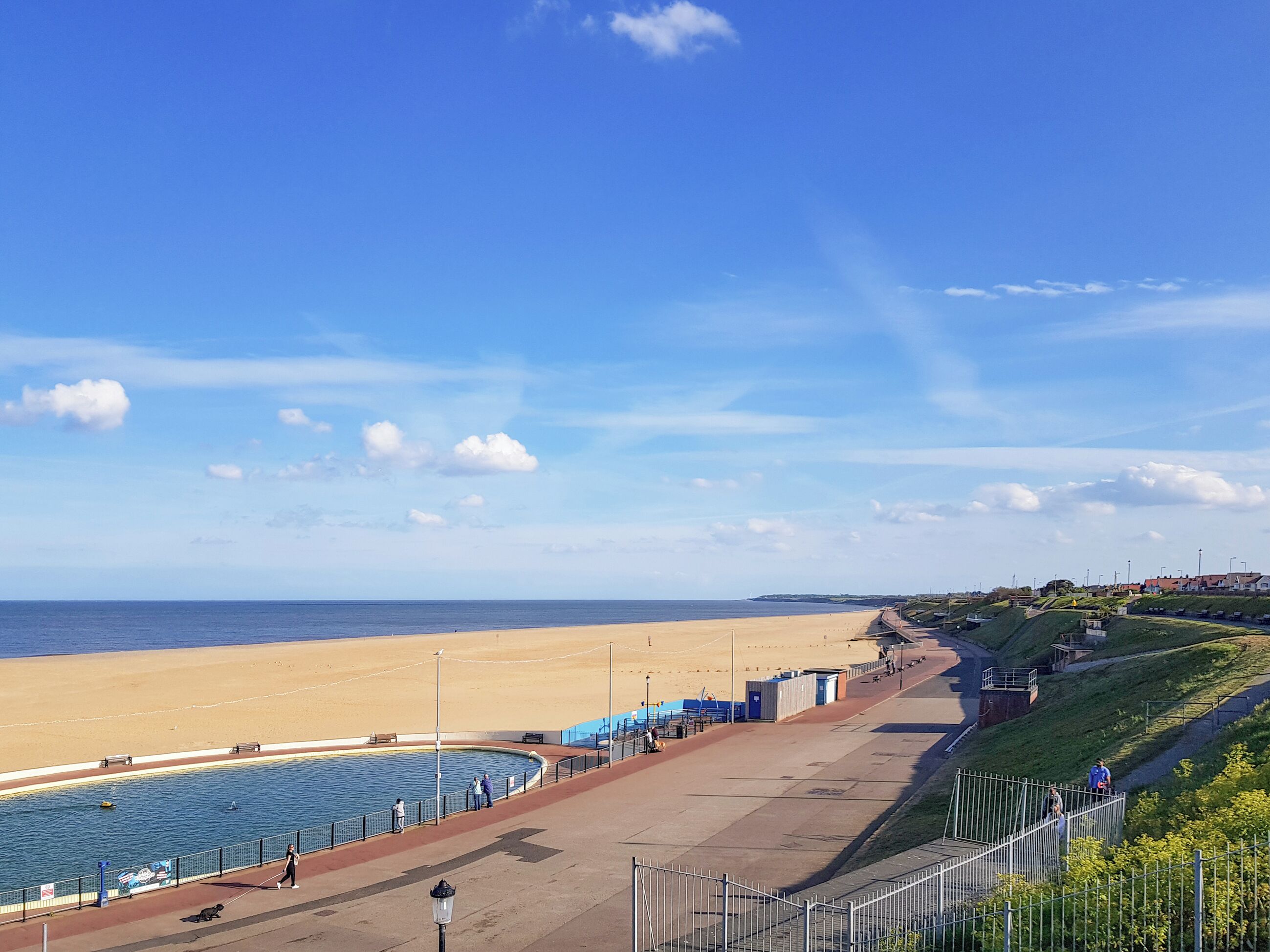Une promenade en bord de mer avec une plage, une piscine et une clôture.