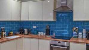 Una cocina con armarios blancos, un salpicadero de azulejos azules, encimera de madera y horno de acero inoxidable.