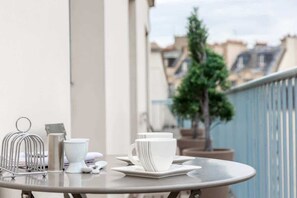 Una mesa dispuesta con tazas y platillos blancos en un balcón con vistas a edificios y un árbol.