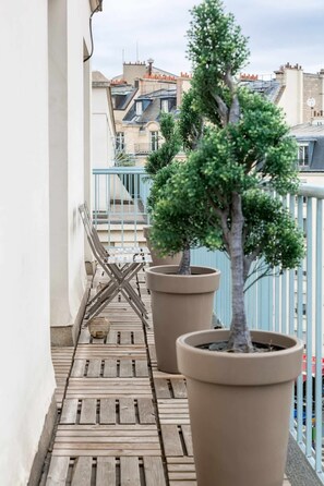 Un balcon doté d’un plancher en bois, de deux grands arbres en pot et d’une rambarde en métal.
