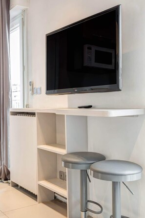 Una sala de estar moderna con un televisor de pantalla plana montado en la pared, una consola blanca y dos taburetes de bar.