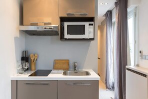 Una cocina compacta con microondas integrado, un lavamanos y una tabla de cortar de madera.