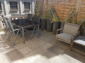 Un patio al aire libre con una mesa y sillas de metal, una silla acolchada y plantas en macetas.