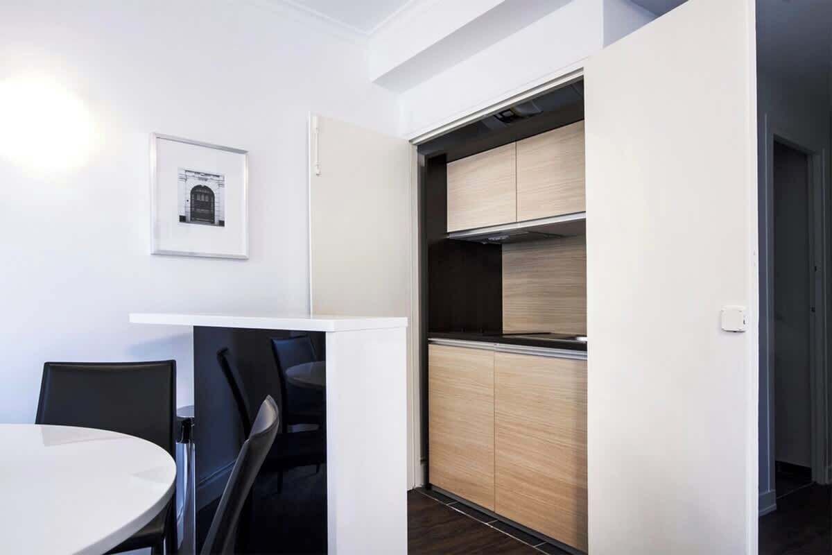 A compact kitchen with a built-in oven and microwave, a dining area with a round table and chairs, and a framed picture on the wall.