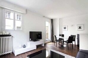 Una sala moderna con televisor de pantalla plana, mobiliario blanco y un comedor con mesa y sillas.